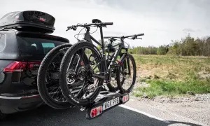 Svart bil med takbox och ett cykelställ för **thule 4 cyklar** redo för äventyr.
