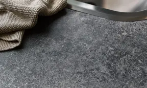 En mörk, stenig laminatskiva med en beige kökshandduk vid diskho.