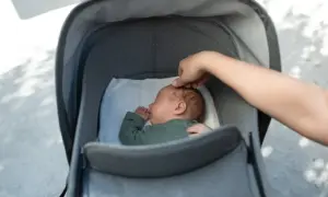 En bebis sover tryggt i en barnkärra. En hand smeker försiktigt barnets huvud.