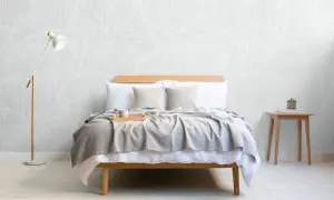 Sovrum med säng, grå pläd, träbricka med mugg och en golvlampa. Vacker tapet med organiskt mönster skapar en lugn boho chic inredning.