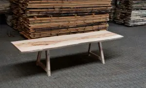 Ett vackert träbord med en unik ådring, redo att bygga ett hem. Staplar av träplankor i bakgrunden.