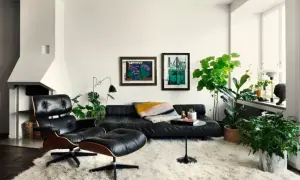 Ett lyxigt vardagsrum med svart lädersoffa, fåtölj och fotpall på en tjock, vit matta. Konst på väggen och många gröna växter.