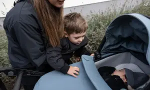 En mamma och ett barn tittar ner på en sovande bebis i en Thule Urban Glide liggdel.