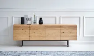 Ett stilrent sideboard i ljust trä med svarta ben, dekorerat med vaser och en lampa.
