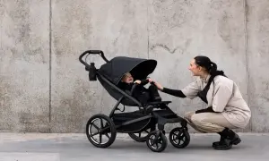 Glad baby i svart cityvagn, en kvinna böjer sig ner för att leka med barnet.