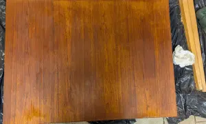 Förbereder för att slipa teakbord. En bit trä ligger på svart plast, bredvid en slipmaskin och en pappersbit.