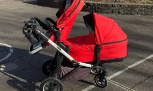 En röd Thule sleek syskonvagn står på en stenlagd uteplats. Vagnen har en liggdel och en sittdel, båda i rött.