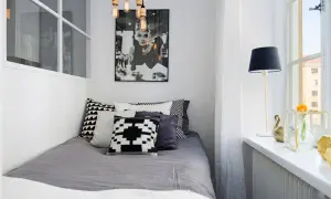 Stilren inredning litet sovrum med Audrey Hepburn-poster, grå sängkläder och grafiska kuddar. En golvlampa och en blomma på fönsterbrädan.