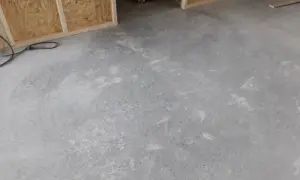 Ett rått betonggolv som väntar på att slipas. Verktyg och byggmaterial syns i bakgrunden.