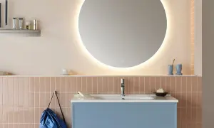 Ett modernt badrum med en blå kommod, rosa kakel och en stor, upplyst rund spegel. En diskret inredning med speglar som skapar rymd.
