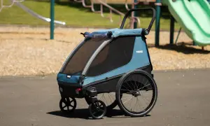 Blå Thule Courier barnvagn med stora hjul står på en asfalterad yta vid en lekplats.