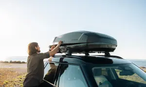Man justerar en Thule lastbox på taket av en bil vid havet.