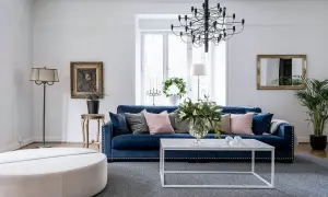 Blå soffa inspiration: En elegant salong med en djupblå sammetssoffa, prydd med kuddar i rosa och grått. Ett modernt soffbord och en stor golvlampa kompletterar rummet.