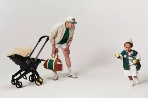 En man med en barnvagn och en sportväska. Barnet leker med tennisbollar. Bältesskydd barnvagn för extra komfort.