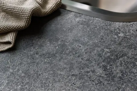 En mörk, stenig laminatskiva med en beige kökshandduk vid diskho.
