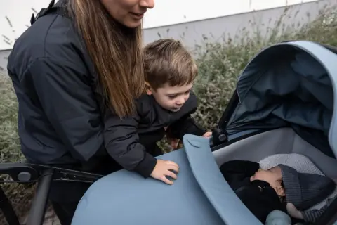 En mamma och ett barn tittar ner på en sovande bebis i en Thule Urban Glide liggdel.