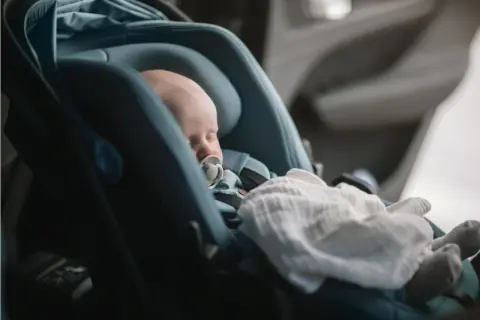 Sovande bebis med napp i en Thule babysitter, tryggt och bekvämt för resan.