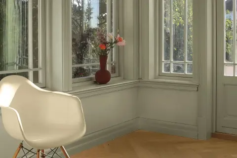 En ljus hall med en vit stol och en vas med blommor på fönsterbrädan. Perfekt måla hall inspiration för en lugn och inbjudande atmosfär.