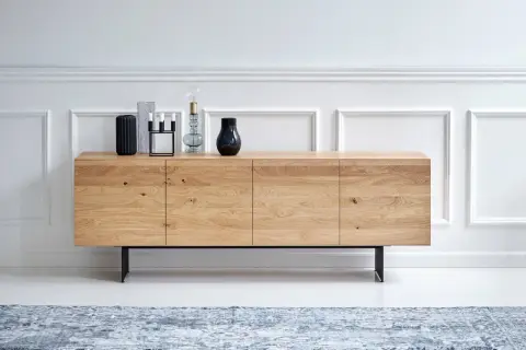 Ett stilrent sideboard i ljust trä med svarta ben, dekorerat med vaser och en lampa.