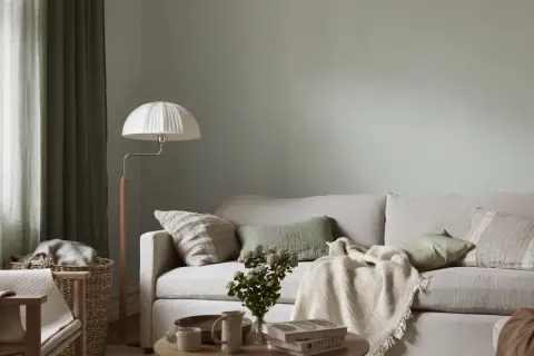 Lugnt och harmoniskt vardagsrum med ljus soffa, gröna kuddar och en vit golvlampa. Perfekt måla vardagsrum inspiration för en avslappnad atmosfär.