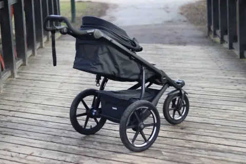 En svart Thule Urban Glide 1 barnvagn står på en träbro. Den är redo för äventyr i stadsmiljö eller på stigar.