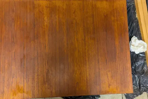 Förbereder för att slipa teakbord. En bit trä ligger på svart plast, bredvid en slipmaskin och en pappersbit.