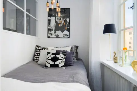 Stilren inredning litet sovrum med Audrey Hepburn-poster, grå sängkläder och grafiska kuddar. En golvlampa och en blomma på fönsterbrädan.