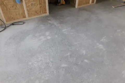 Ett rått betonggolv som väntar på att slipas. Verktyg och byggmaterial syns i bakgrunden.