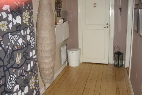 En inreda långsmal hall med en stor golvlampa, en vit dörr och en svart lykta.
