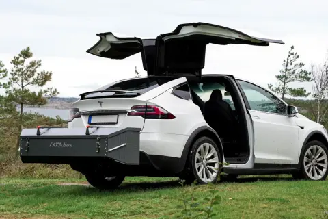 Vit Tesla Model X med bakluckan och dörrarna öppna. En smal takbox, IXTA box, är monterad baktill.