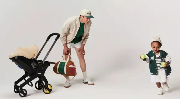 En man med en barnvagn och en sportväska. Barnet leker med tennisbollar. Bältesskydd barnvagn för extra komfort.