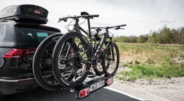 Svart bil med takbox och ett cykelställ för **thule 4 cyklar** redo för äventyr.