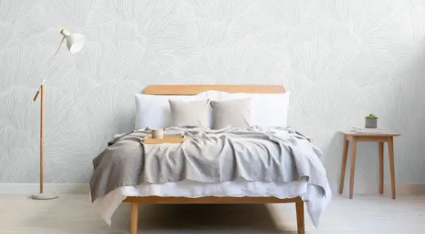 Sovrum med säng, grå pläd, träbricka med mugg och en golvlampa. Vacker tapet med organiskt mönster skapar en lugn boho chic inredning.