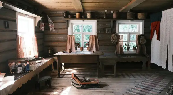 Mysigt torp inredning med träväggar, fönster med blommor och dukar, samt textilier som skapar en varm atmosfär.