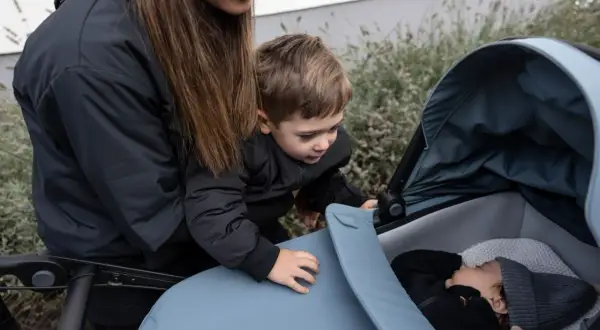 En mamma och ett barn tittar ner på en sovande bebis i en Thule Urban Glide liggdel.
