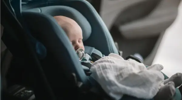 Sovande bebis med napp i en Thule babysitter, tryggt och bekvämt för resan.
