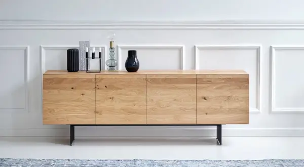 Ett stilrent sideboard i ljust trä med svarta ben, dekorerat med vaser och en lampa.