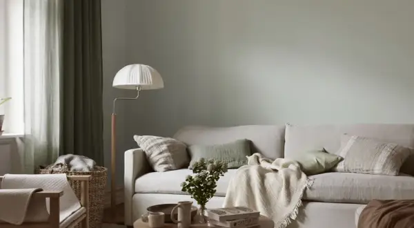 Lugnt och harmoniskt vardagsrum med ljus soffa, gröna kuddar och en vit golvlampa. Perfekt måla vardagsrum inspiration för en avslappnad atmosfär.