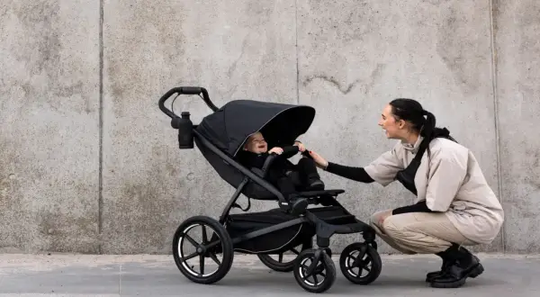 Glad baby i svart cityvagn, en kvinna böjer sig ner för att leka med barnet.