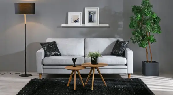 Ett stilrent grått och beige vardagsrum med en ljus soffa, svarta kuddar, träbord och en stor grön växt.