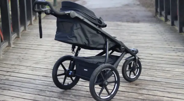 En svart Thule Urban Glide 1 barnvagn står på en träbro. Den är redo för äventyr i stadsmiljö eller på stigar.