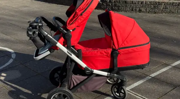 En röd Thule sleek syskonvagn står på en stenlagd uteplats. Vagnen har en liggdel och en sittdel, båda i rött.