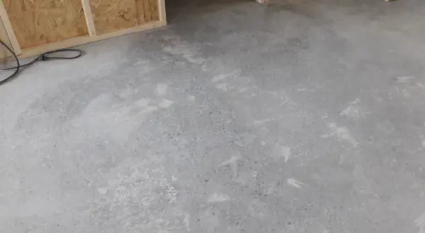 Ett rått betonggolv som väntar på att slipas. Verktyg och byggmaterial syns i bakgrunden.