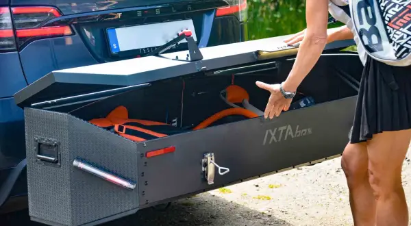 En person packar ner utrustning i en robust låda, en av många praktiska Thule produkter, fäst på en Tesla.