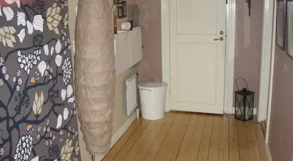 En inreda långsmal hall med en stor golvlampa, en vit dörr och en svart lykta.