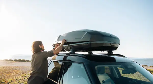 Man justerar en Thule lastbox på taket av en bil vid havet.