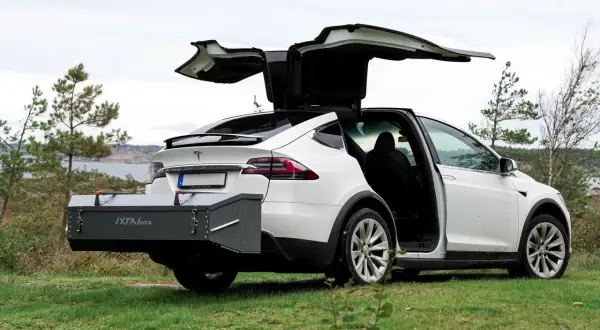 Vit Tesla Model X med bakluckan och dörrarna öppna. En smal takbox, IXTA box, är monterad baktill.
