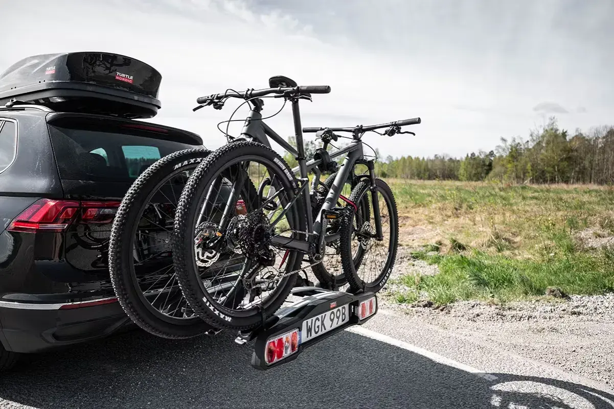 Svart bil med takbox och ett cykelställ för **thule 4 cyklar** redo för äventyr.