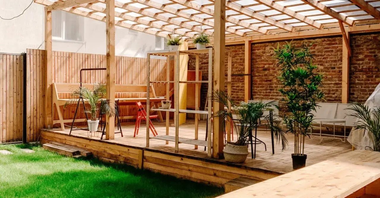 En mysig uteplats med träpergola, bänkar och växter. Perfekt för att måla tryckimpregnerat trä och njuta av sommaren.