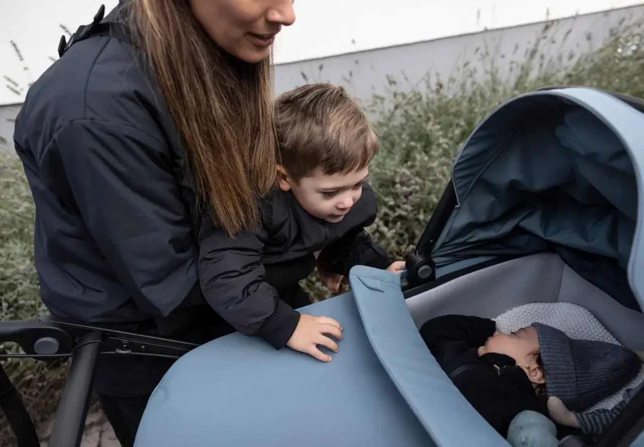En mamma och ett barn tittar ner på en sovande bebis i en Thule Urban Glide liggdel.